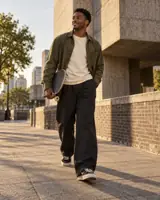AI illustration of a Black man holding a skateboard on a sunlit city street, shown full length.